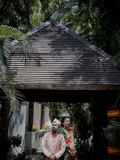 A dramatic portrait of a couple at the entrance of a resort, framed by lush greenery and interesting shadows.