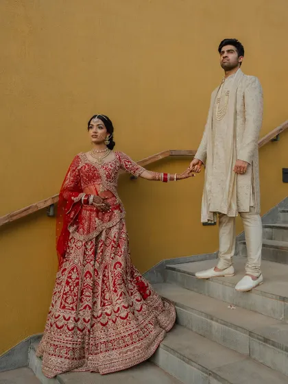 A regal portrait of the couple in their stunning red and cream wedding attire. We use architectural elements like staircases to add a touch of grandeur to our compositions.