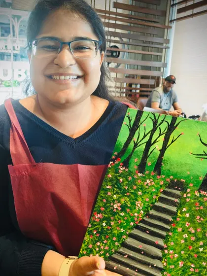 A smiling artist with her completed painting of a path through a forest in bloom. A testament to what beginners can achieve.
