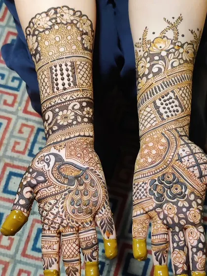 A beautiful example of a peacock-centric design. The main motif on the palm is a large, detailed peacock, with its feathers flowing into intricate floral and geometric patterns that extend up the arm.