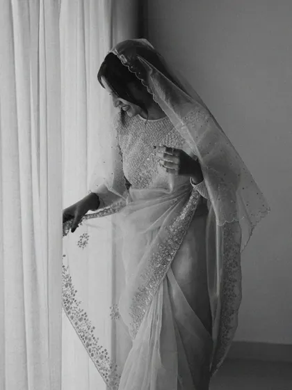 A bride in black and white, admiring the delicate embroidery on her saree. This quiet, personal moment is full of grace and appreciation for the details of her attire.