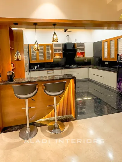 A full view of the open kitchen with its breakfast bar, showcasing the harmonious blend of dark granite, wood tones, and light-colored cabinets.