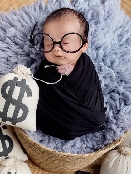 The boss is sleeping on the job! This hilarious 'Boss Baby' theme features a newborn in a basket surrounded by prop money bags and wearing oversized glasses.