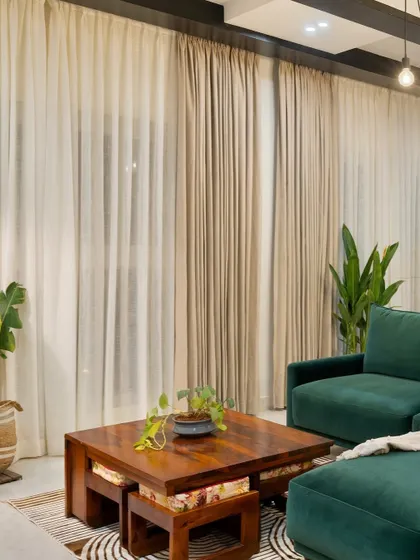 A closer look at the industrial-chic living space we designed. The combination of an emerald green sofa, warm wood coffee table, and sheer curtains creates a perfect balance of raw textures and refined comfort.