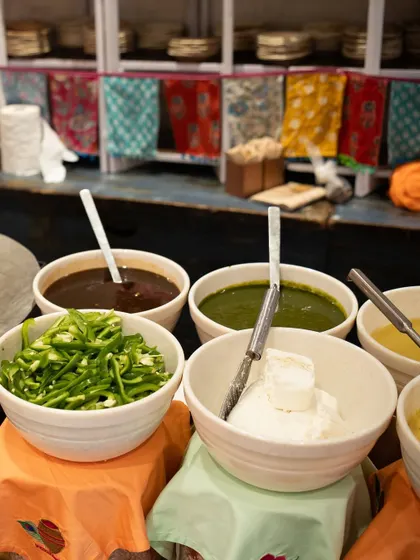 The essential components of great Indian food. Bowls of tangy tamarind chutney, fresh green chutney, spicy chilies, and creamy yogurt, ready to accompany our delicious snacks.