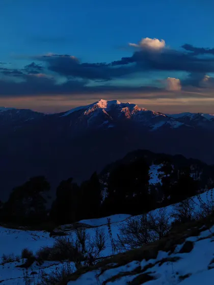The last light of the sun kisses the top of a snowy peak. This fleeting moment, known as alpenglow, paints the mountain in a soft, warm light against the darkening sky.