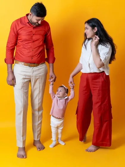 A family helps their little one take her first steps. This photo, set against a vibrant yellow background, is full of color, movement, and joy.