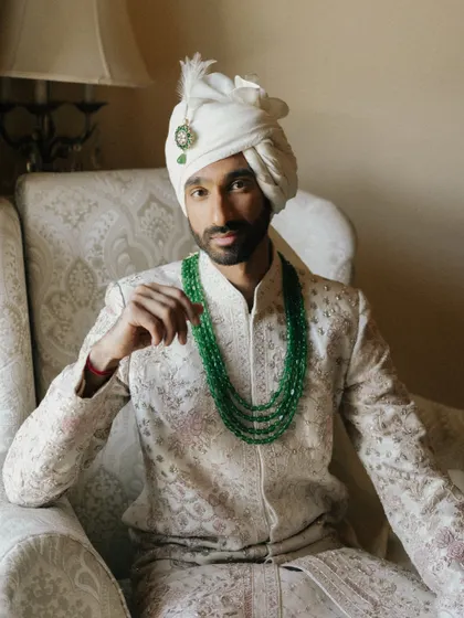A regal portrait of the groom, his emerald necklace adding a touch of color to the classic ivory sherwani. I focus on capturing the quiet confidence and poise of the groom on his wedding day.
