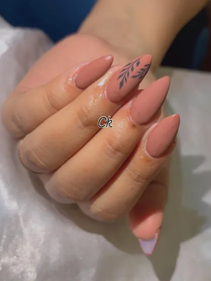 A chic and minimalist design featuring a matte nude polish with a simple, hand-painted black leaf accent.