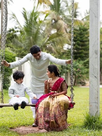 A playful moment with a father pushing his two children on a swing in the garden, all dressed in matching traditional wear.