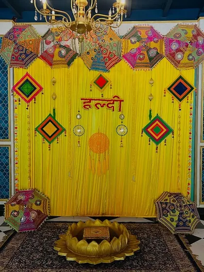 A traditional Haldi backdrop with bright yellow drapes, Rajasthani umbrellas, and colorful hangings, perfect for a classic and festive celebration.
