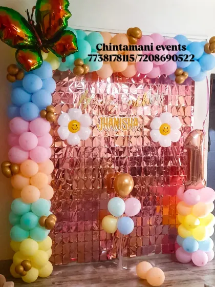 A first birthday backdrop combines pastel balloons, pink sequins, a butterfly foil and personalised birthday lettering.