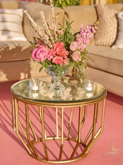 A close-up of a gold-framed coffee table, holding a beautiful arrangement of pink roses and baby's breath, with the soft glow of candles beside it.