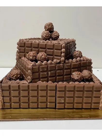 A spectacular three-tier square cake for a true chocolate lover, covered in chocolate bars and topped with Ferrero Rocher.