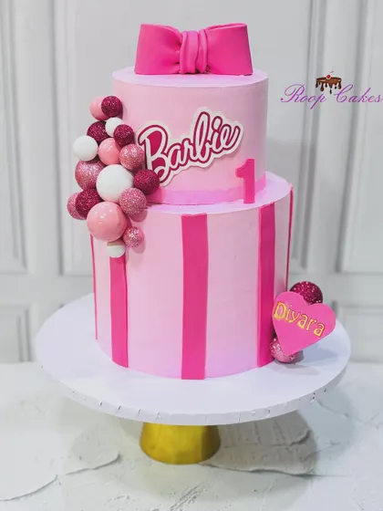One year of magic and sweetness. This two-tier Barbie cake is perfect for a little princess's first birthday, with pink stripes, a big bow, and lots of sparkle.