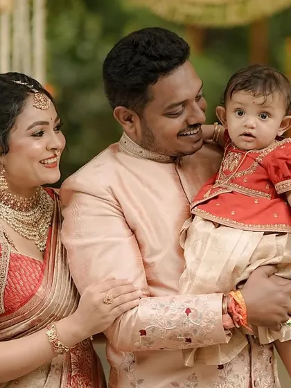 A close-up of a family sharing a happy moment. The intricate embroidery on the mother's red blouse and the father's jacket highlights the detailed craftsmanship that goes into our family twinning collections.