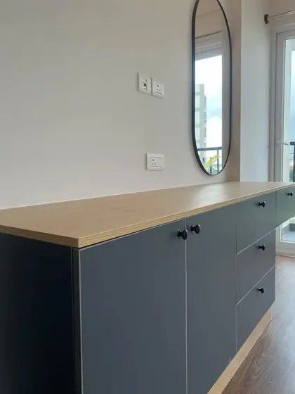 A modern sideboard in grey and light wood, with a sleek oval mirror. This versatile piece can serve as a dresser in a bedroom or a console table in a living area.