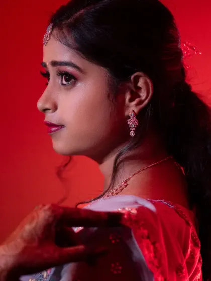 A profile shot under dramatic red lighting, perfect for a bold reception look. The makeup is defined and sharp, with a focus on the eyes and a strong lip color to create a memorable portrait.