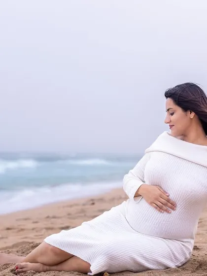 A moment of peace. The mom-to-be sits by the water's edge, creating a serene and contemplative portrait in a cozy white knit dress.