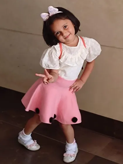 A chic and modern two-piece look. This outfit pairs a white top with delicate ruffles and puff sleeves with a stylish pink skirt featuring black polka dot accents.