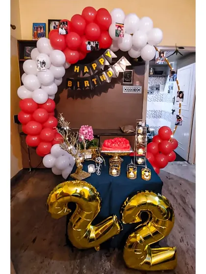 We help you celebrate every milestone, like this 22nd birthday. This cozy home setup features large gold foil balloon numbers, a red and white balloon arch, and a decorated table ready for the cake cutting.