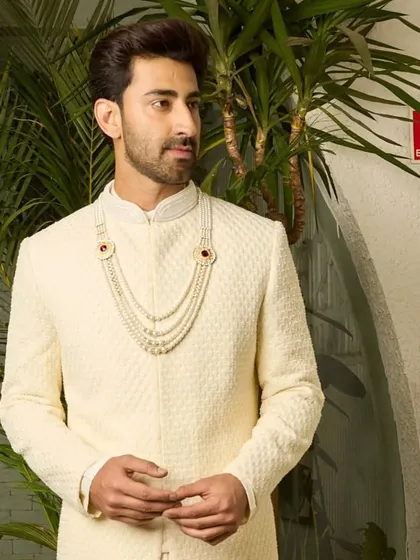 This shot captures the regal bearing of the off-white sherwani. The textured fabric and perfect fit create a silhouette that is both traditional and modern.