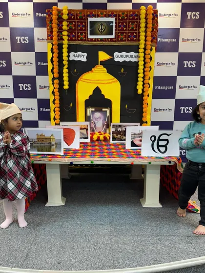 Two girls stand respectfully before the Gurpurab display. We create an environment where children can learn about and appreciate different religious traditions.