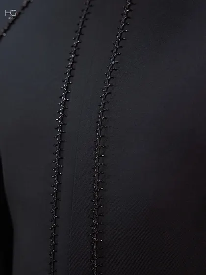A close-up of the delicate, hand-stitched beading that runs down the back of the achkan, adding a hint of sparkle to the deep black fabric.