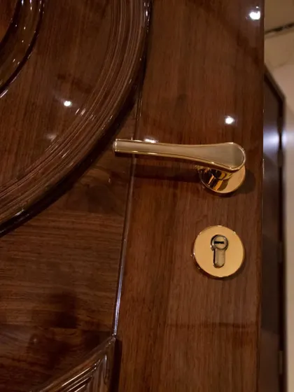 A close-up of a high-gloss solid wood door, showing the flawless finish and the classic gold hardware.