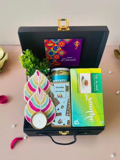 A perfect example of an affordable yet elegant corporate gift. This black suitcase hamper, priced under ₹1000, includes a beaded t-light holder, green tea, and snacks.