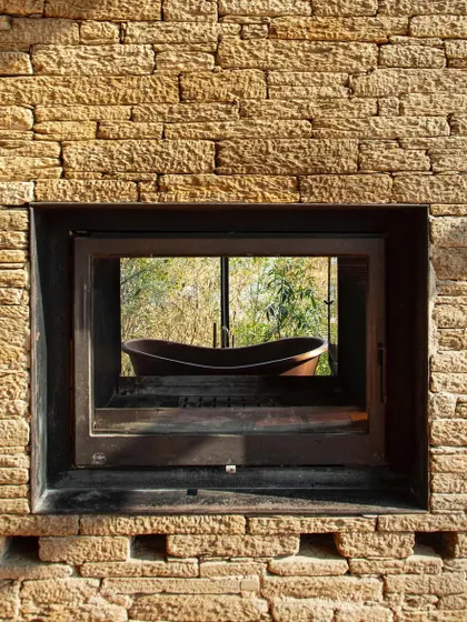 A window at the Himalayan home frames a view of an outdoor bathtub, blending the intimate act of bathing with a direct connection to the rugged, natural setting.