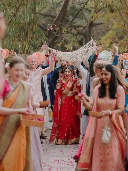 The bride's joyful entrance under the phoolon ki chaadar, surrounded by smiling friends and family. This shot is full of energy and happiness.
