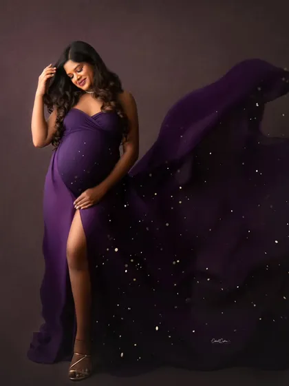 A quiet, beautiful moment. The mom-to-be looks down at her bump, her purple gown sparkling with a magical dust effect.
