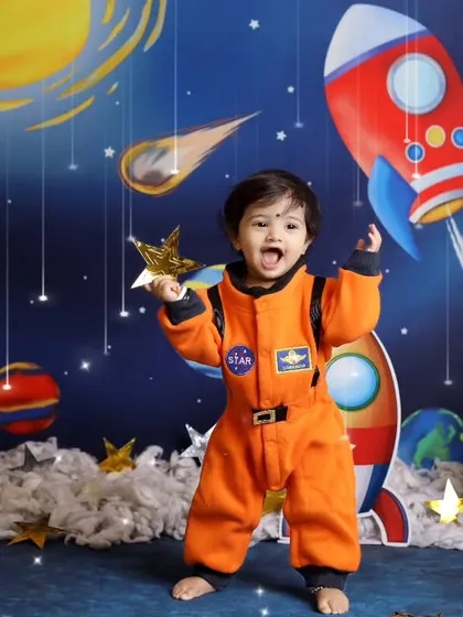 3, 2, 1, blast off! This little astronaut is ready for an adventure in our outer space themed photoshoot, complete with a NASA jumpsuit and a backdrop of planets and rockets.