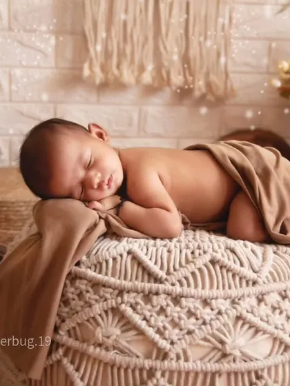 A beautiful shot of a baby sleeping on a woven macrame pouf. This pose highlights the baby's delicate features against the detailed, textured surface.