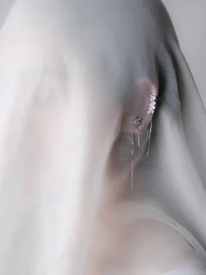 An artistic and mysterious portrait for a jewellery shoot, with the model's face partially veiled by a sheer white cloth. This focuses attention on the delicate earring and creates an ethereal mood.