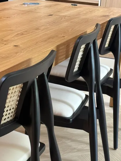 A detailed shot of my custom dining chairs, featuring a black finish, white upholstered seat, and a natural cane backrest insert. This design combines modern aesthetics with traditional materials for a sophisticated restaurant look.