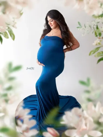 A dreamy and artistic solo portrait. The beautiful mom-to-be in her blue gown is surrounded by a soft, floral overlay, making the photo feel magical and special.