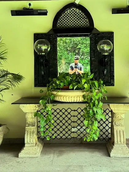 An antique-style console table and mirror, paired with lush indoor plants, create a classic and elegant feel in this covered patio area in New Friends Colony.