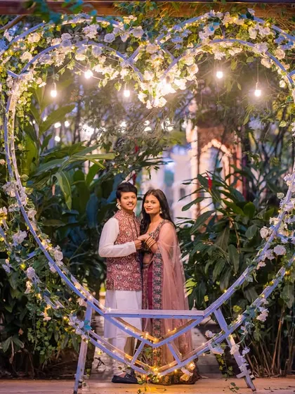 A beautiful portrait of a couple framed by a heart-shaped arch decorated with white flowers and lights. This is a classic and romantic pre-wedding setup.
