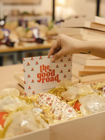 Adding our signature "The Good Road" card to a hamper. It's our seal of quality and care, letting the recipient know their gift was curated by us.