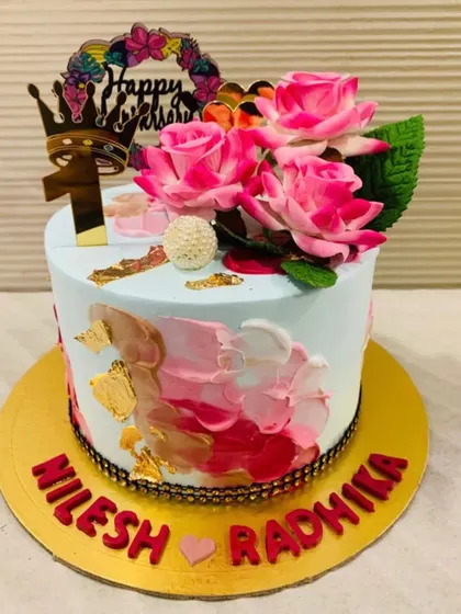 A beautiful anniversary cake celebrating one year together. The design features a mix of pink and gold brushstrokes, topped with lovely pink roses and a crown.