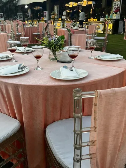 A beautiful outdoor table setting with peach-colored linens and transparent chairs. The simple decor allows the natural beauty of the surroundings to shine through.
