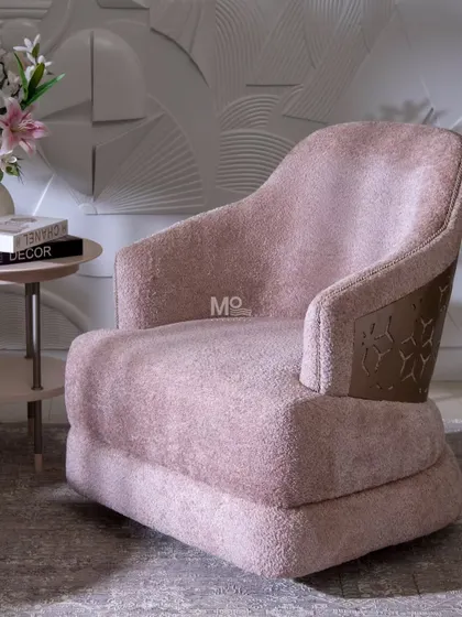 The Blush Haven Armchair, where plush textures meet architectural grace. Upholstered in a blush bouclé, its defining feature is the precision-cut metal detail with a geometric motif, inspired by ornamental latticework.