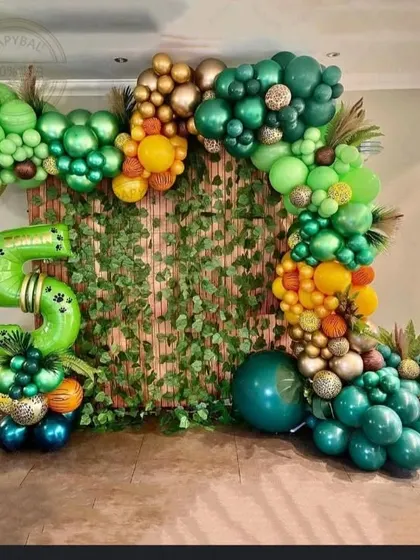 An organic balloon arch designed to look like a lush jungle vine. I used various shades of green, gold, and orange balloons, along with a large number '5' foil balloon, against a bamboo-style backdrop.