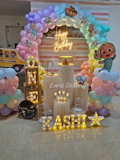 A Cocomelon setup featuring a full circular balloon arch in beautiful pastel colors. The neon "Happy Birthday" sign and light-up name add a special touch.