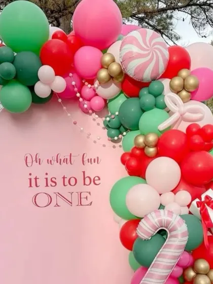 "Oh what fun it is to be ONE!" A sweet and unique Christmas-themed first birthday. This design uses a soft pink backdrop with festive red, green, and candy-striped balloons.