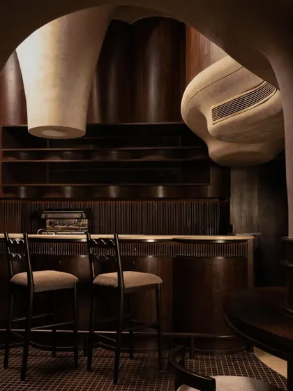 The bar at Call Me Ten, where sculptural forms descend from the ceiling, housing ventilation and lighting. This detail highlights the fusion of function and artistry, with dark wood and stone creating a rich, tactile experience.