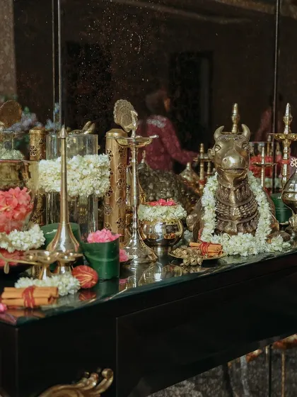 A wide shot of the puja table, reflecting in a mirror. The arrangement includes brass statues, floral garlands, and traditional lamps, creating a beautiful and serene atmosphere for the ceremony.