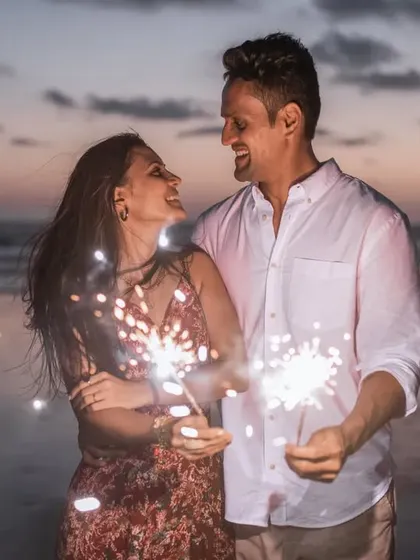 A joyful shot of the couple laughing and enjoying the sparklers during their beach pre-wedding shoot.